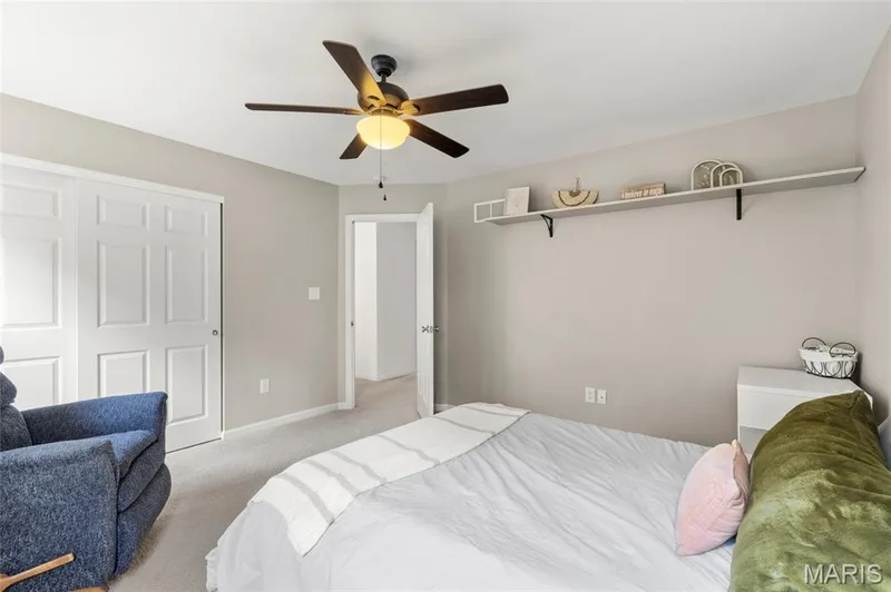 Second Bedroom featuring neutral wall tones, wall shelving, carpeted flooring, a ceiling fan with integrated lighting, and two windows with blinds. — 921 Molloy Drive, O'Fallon, MO 63366