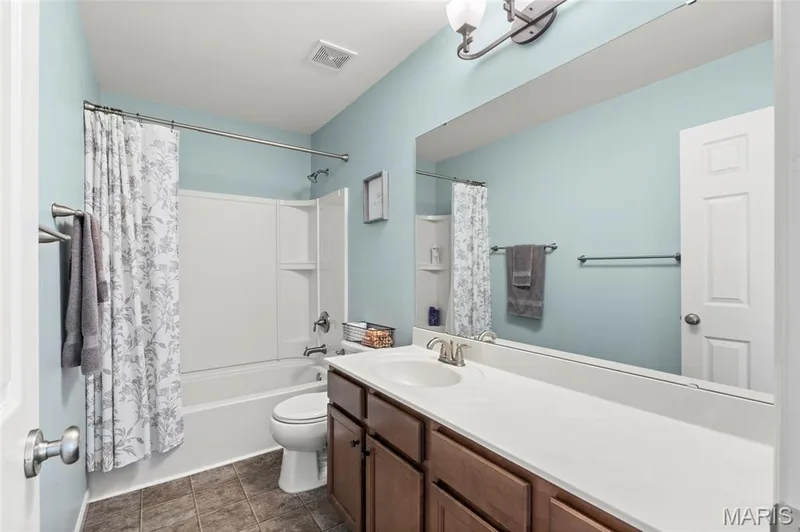 Shared Bathroom featuring a spacious vanity with an integrated sink, extended countertop, wood-finish cabinetry, and a full-width mirror — 921 Molloy Drive, O'Fallon, MO 63366