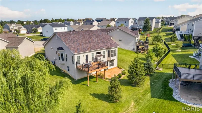 Backyard featuring a manicured lawn, mature trees, and a composite deck with black railings — 713 Bellingrath Gardens Court, Wentzville, MO 63385