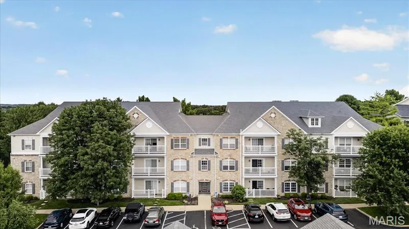Multi-story building featuring stone and siding exterior, multiple balconies with white railings, dormer windows, and a dedicated parking area — 5 Monarch Trace Court #108, Chesterfield, MO 63017
