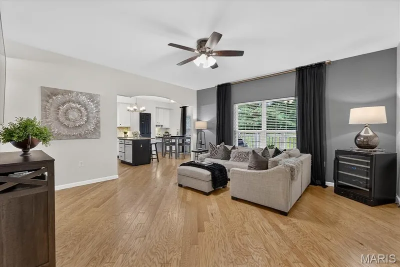 Open-concept living area featuring wood-finish flooring, a ceiling fan, and a wide window with blinds — 5 Monarch Trace Court #108, Chesterfield, MO 63017