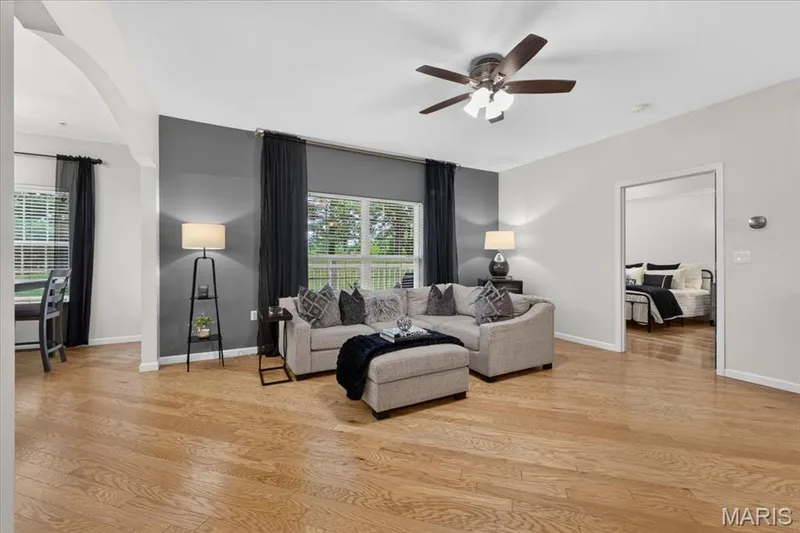 Spacious living area featuring wood-finish flooring, a ceiling fan with integrated lighting, and a prominent accent wall — 5 Monarch Trace Court #108, Chesterfield, MO 63017