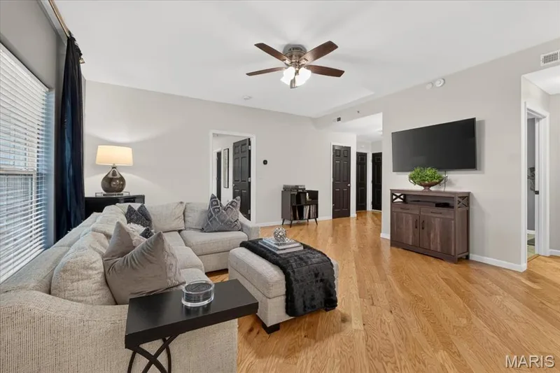 Bright interior featuring wood-finish flooring, a ceiling fan with integrated lighting, and multiple windows with blinds — 5 Monarch Trace Court #108, Chesterfield, MO 63017