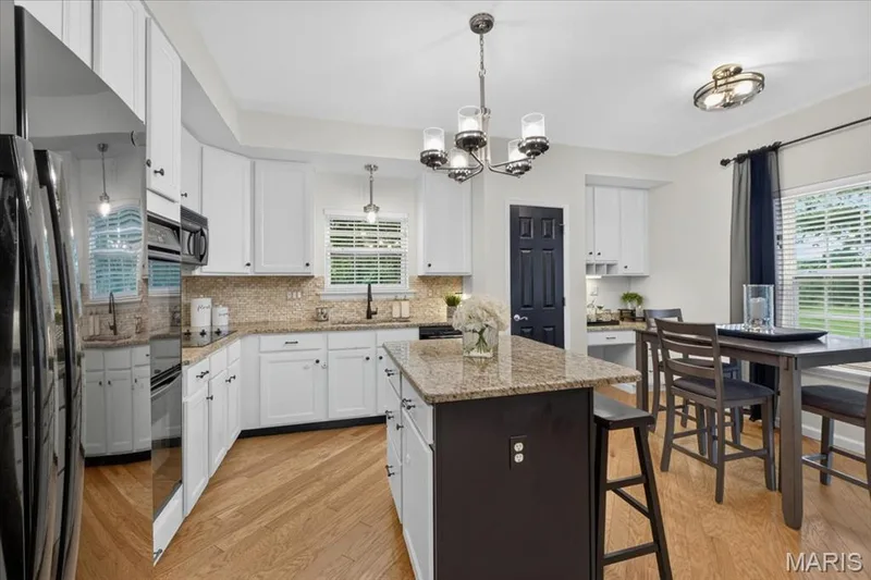 Kitchen featuring wood-finish flooring, white cabinetry, a stone-finish island countertop, built-in microwave, and pendant lighting — 5 Monarch Trace Court #108, Chesterfield, MO 63017