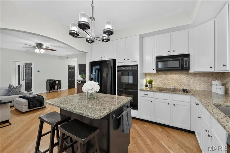 Kitchen featuring white cabinetry, dark island with seating, built-in double oven, and granite countertops — 5 Monarch Trace Court #108, Chesterfield, MO 63017