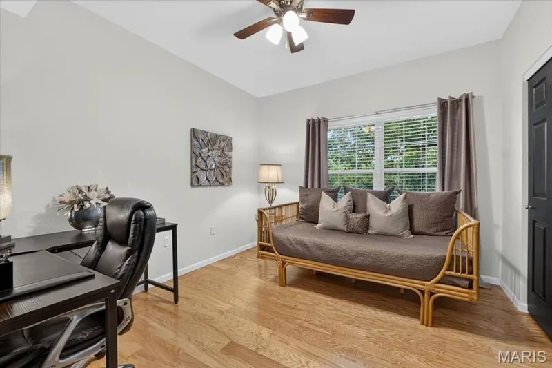 Bright interior space featuring wood-finish flooring, a ceiling fan with integrated lighting, and a window with blinds and drapes — 5 Monarch Trace Court #108, Chesterfield, MO 63017