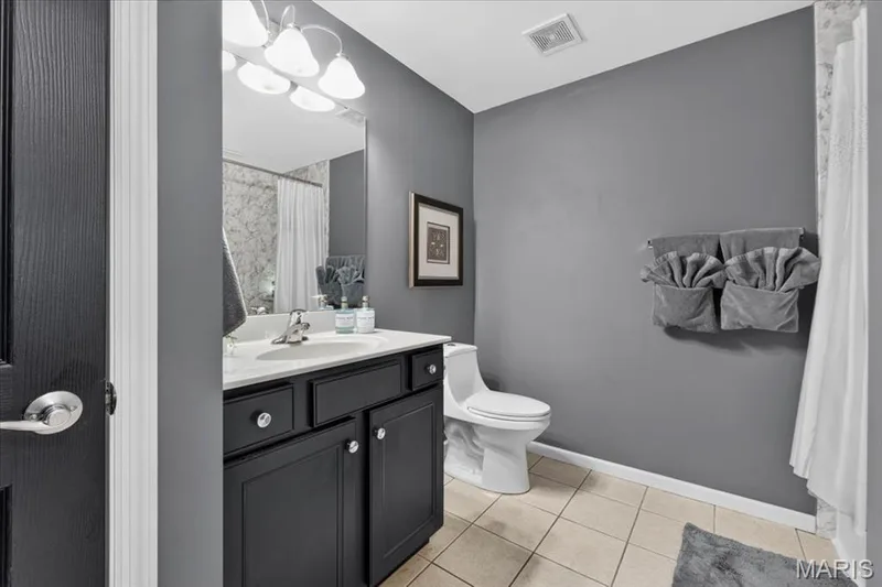 Bathroom featuring a dark wood-finish vanity with a light-toned countertop, a wall-mounted mirror, and a modern toilet — 5 Monarch Trace Court #108, Chesterfield, MO 63017