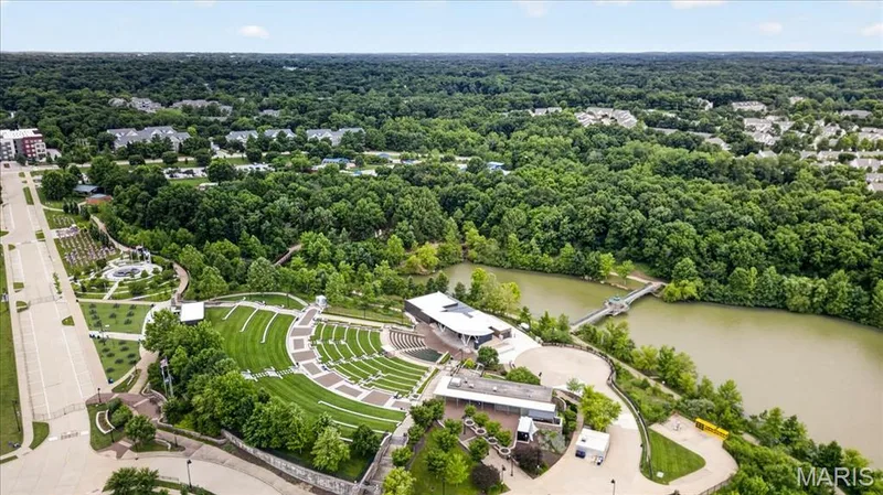 Amphitheater with tiered lawn seating, bordered by a waterway with a pedestrian bridge, and surrounded by mature trees — 5 Monarch Trace Court #108, Chesterfield, MO 63017
