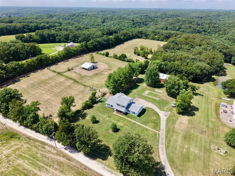 Expansive property featuring the primary residence, large pole barn, 4 stall horse barn, private pond, paved drive, and open fields surrounded by dense natural landscaping — 33 Timber Ridge Drive, Marthasville, MO 63357