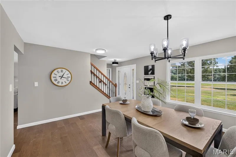 Luxury flooring throughout, featuring a modern chandelier, large windows, a staircase with wood railings, and a front entry door with decorative glass — 33 Timber Ridge Drive, Marthasville, MO 63357