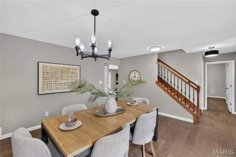 Dining area featuring luxury flooring, a contemporary chandelier, and a visible staircase with wood banister and wrought iron spindles — 33 Timber Ridge Drive, Marthasville, MO 63357