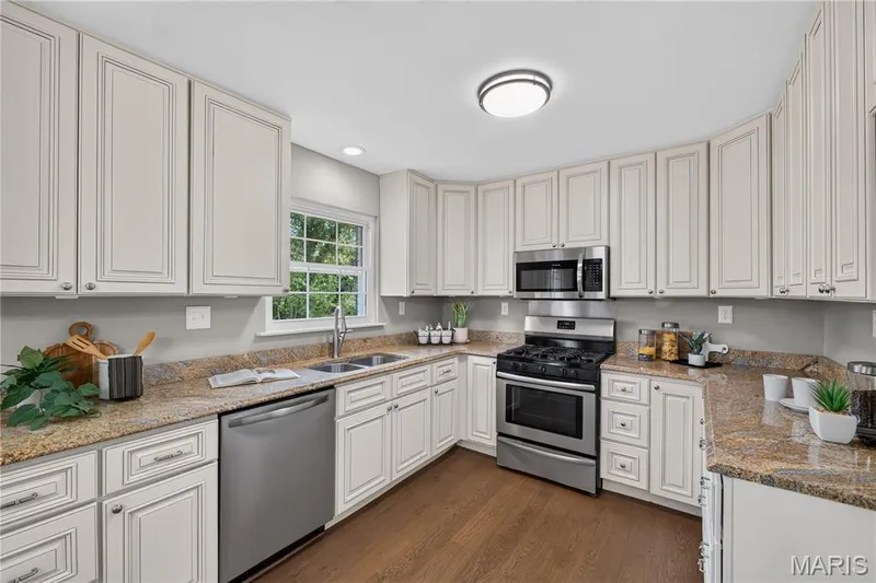Kitchen featuring extensive white cabinetry, stainless steel appliances, speckled stone countertops, a double basin sink, and wood-finish flooring — 33 Timber Ridge Drive, Marthasville, MO 63357