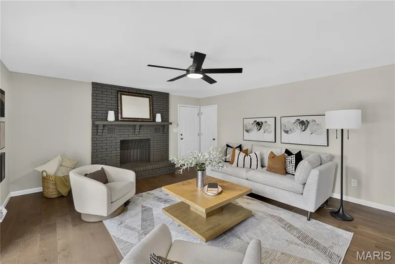 Living area featuring a brick fireplace with a mantel, wood-finish flooring, light-toned walls, a ceiling fan with integrated lighting, and white paneled doors — 33 Timber Ridge Drive, Marthasville, MO 63357