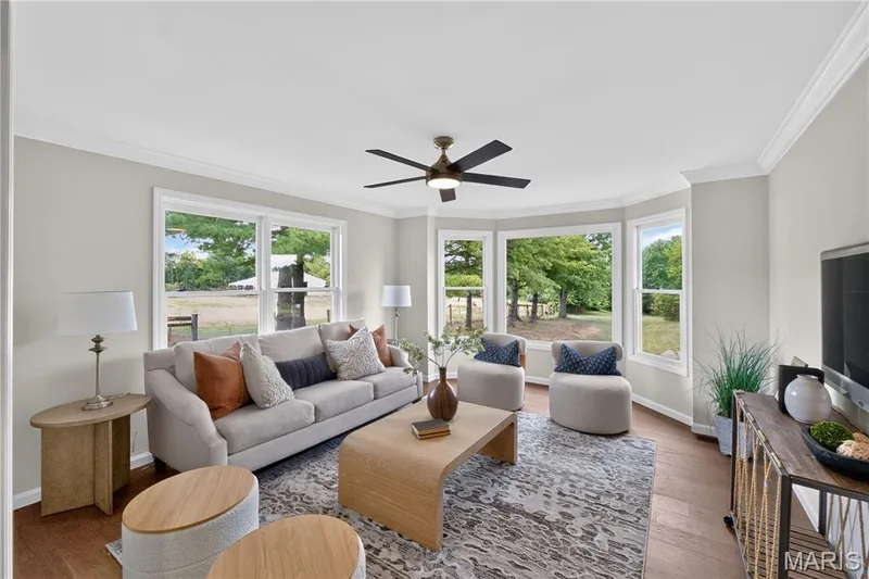 Sun room off of primary suite featuring expansive bay windows, wood-finish flooring, a ceiling fan with integrated lighting, crown molding, and neutral wall tones — 33 Timber Ridge Drive, Marthasville, MO 63357