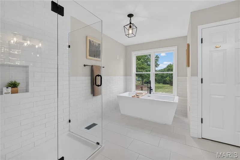 Luxury updated primary suite bath, with freestanding soaking tub, modern fixtures, with a contemporary black wall-mounted faucet, complemented by a glass-enclosed shower featuring subway tile surround and a built-in niche — 33 Timber Ridge Drive, Marthasville, MO 63357