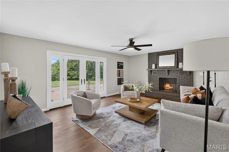 Living area featuring a painted brick fireplace, wood-finish flooring, and a ceiling fan — 33 Timber Ridge Drive, Marthasville, MO 63357