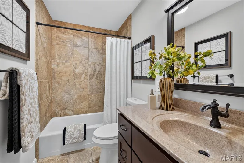 Bathroom featuring a spacious tub, tiled shower surround with decorative accent band, integrated sink with a light-toned countertop, dark wood-finish vanity, and a large framed mirror — 33 Timber Ridge Drive, Marthasville, MO 63357