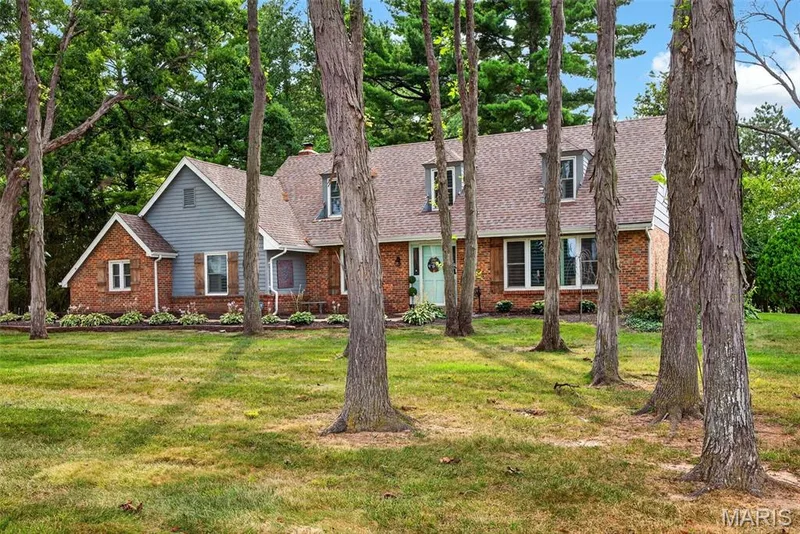 Brick and siding exterior featuring a prominent front lawn with mature trees — 4 Chantilly Court, Lake St. Louis, MO 63367