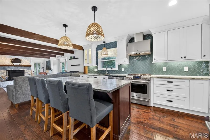 Open-concept kitchen featuring a large island with seating, stainless steel appliances, white cabinetry, and a herringbone-patterned tile backsplash — 4 Chantilly Court, Lake St. Louis, MO 63367