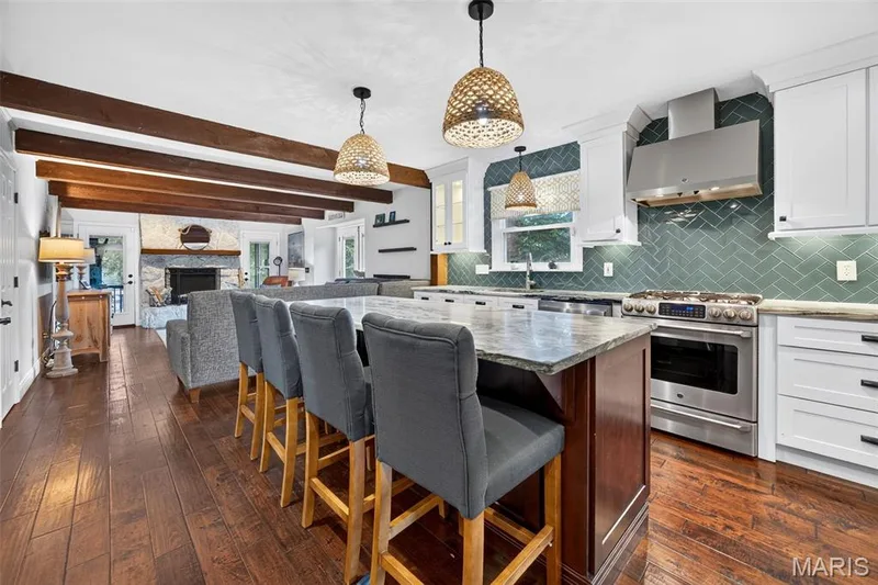 Gourmet kitchen featuring a large island with stone countertop, stainless steel appliances, white cabinetry with dark hardware, and a teal herringbone tile backsplash — 4 Chantilly Court, Lake St. Louis, MO 63367