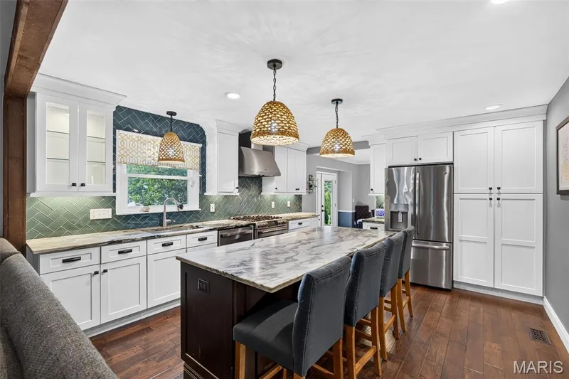 Kitchen featuring a large central island with seating, white cabinetry, integrated stainless steel appliances, and wood-finish flooring — 4 Chantilly Court, Lake St. Louis, MO 63367