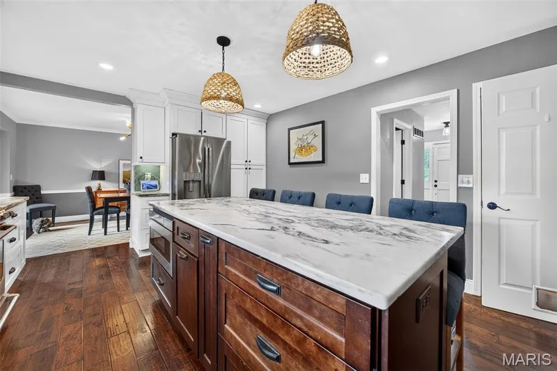 Kitchen featuring a large island with a marbled countertop, rich wood-finish flooring, white upper cabinetry, stainless steel refrigerator, and recessed lighting — 4 Chantilly Court, Lake St. Louis, MO 63367
