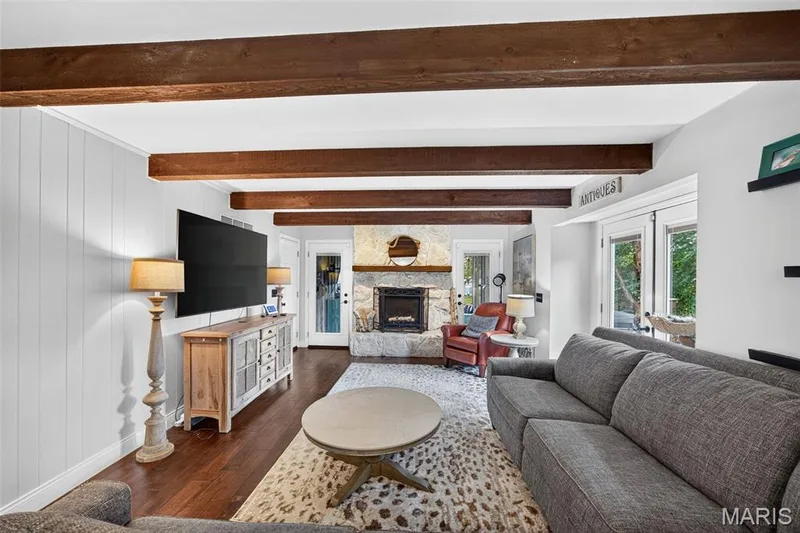 Living area featuring exposed ceiling beams, wood-finish flooring, a stone fireplace, and French doors — 4 Chantilly Court, Lake St. Louis, MO 63367
