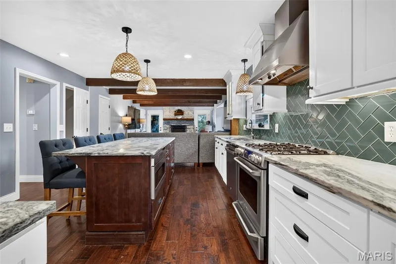 Kitchen featuring a gas range, stainless steel appliances, herringbone tile backsplash, white cabinetry, and wood-finish flooring — 4 Chantilly Court, Lake St. Louis, MO 63367
