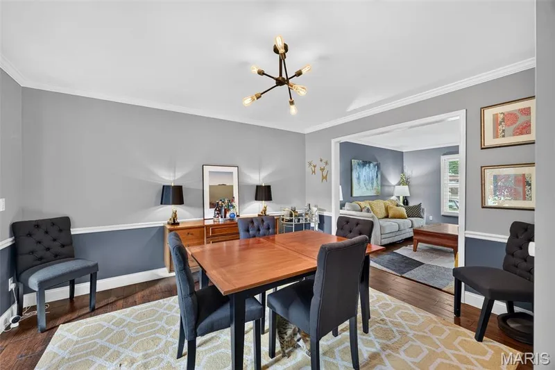 Dining area featuring wood-finish flooring, two-tone wall treatment, crown molding, and a contemporary light fixture — 4 Chantilly Court, Lake St. Louis, MO 63367