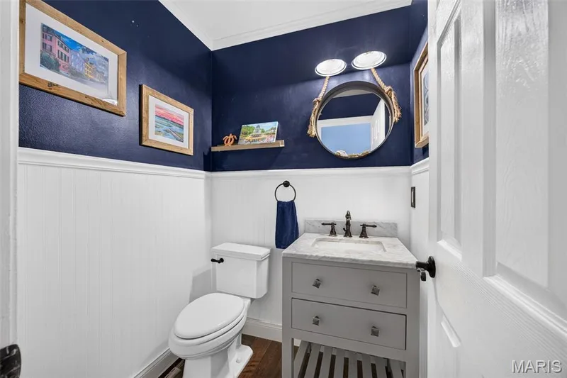 Hall main floor 1/2 bath powder room featuring board and batten wainscoting, a vanity with a stone countertop, bronze-finish fixtures, and wood-finish flooring — 4 Chantilly Court, Lake St. Louis, MO 63367