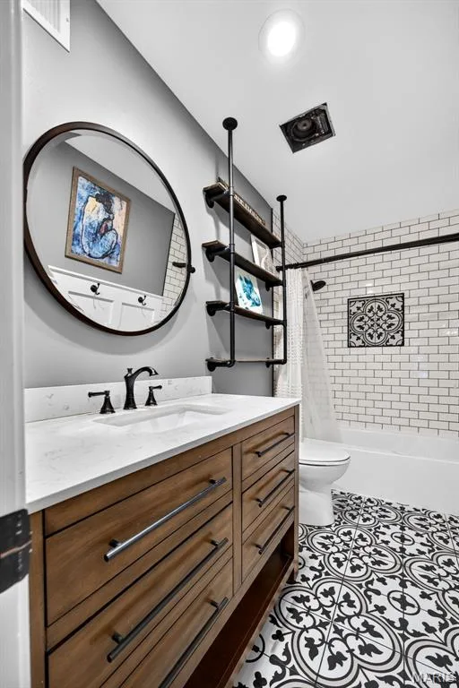 Upstairs Hall Shared Bathroom featuring a wood-finish vanity with a white countertop and integrated sink, matte black faucet, and a round wall mirror — 4 Chantilly Court, Lake St. Louis, MO 63367
