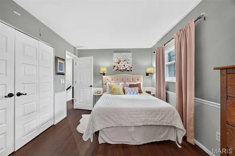 Bedroom #2 featuring dark wood-finish flooring, two sets of white bifold closet doors, a single window, and a white baseboard with chair rail molding — 4 Chantilly Court, Lake St. Louis, MO 63367
