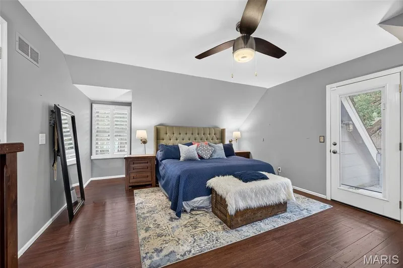 Spacious primary bedroom room featuring wood-finish flooring, a contemporary ceiling fan, and a built-in window with white plantation shutters — 4 Chantilly Court, Lake St. Louis, MO 63367