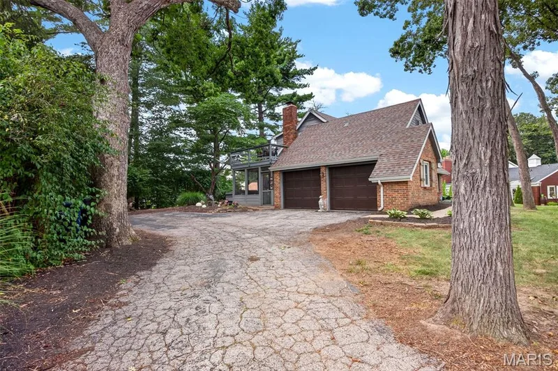 Brick-front residence featuring a two-car garage with dark wood-finish doors, a prominent brick chimney, and a multi-level roofline — 4 Chantilly Court, Lake St. Louis, MO 63367