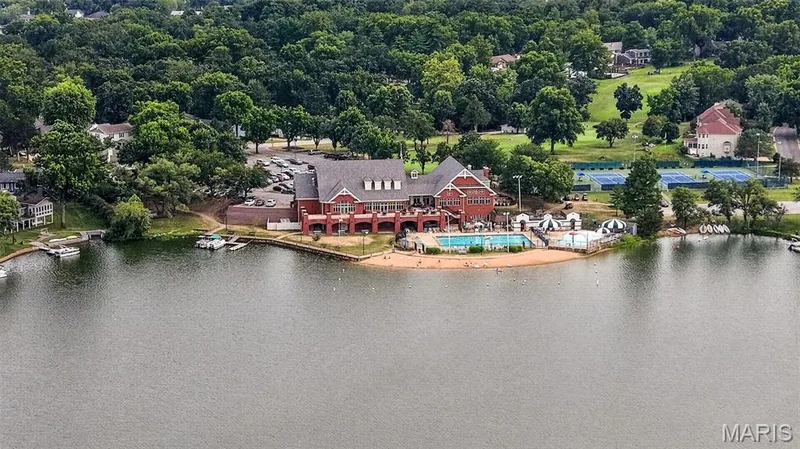 Lakeside property featuring a red brick building with multiple gables, a swimming pool, sandy beach area, tennis courts, and boat docks — 4 Chantilly Court, Lake St. Louis, MO 63367
