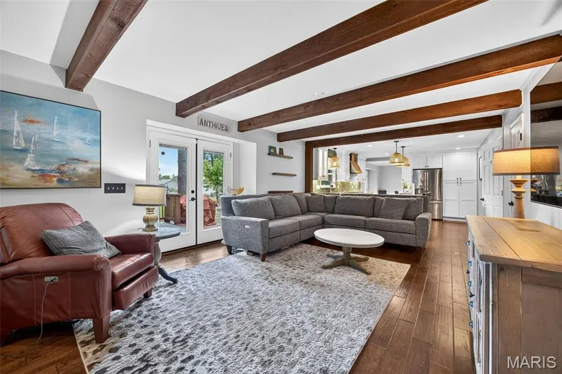 Open-concept living area featuring wood-finish flooring, exposed ceiling beams, and white walls — 4 Chantilly Court, Lake St. Louis, MO 63367
