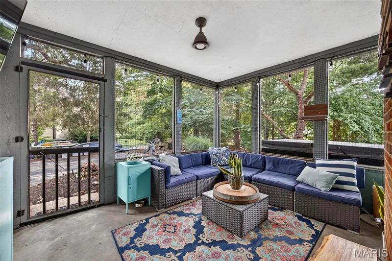 Spacious screened porch featuring a ceiling fan, exposed brick wall section, concrete flooring, and an exterior door with railing — 4 Chantilly Court, Lake St. Louis, MO 63367