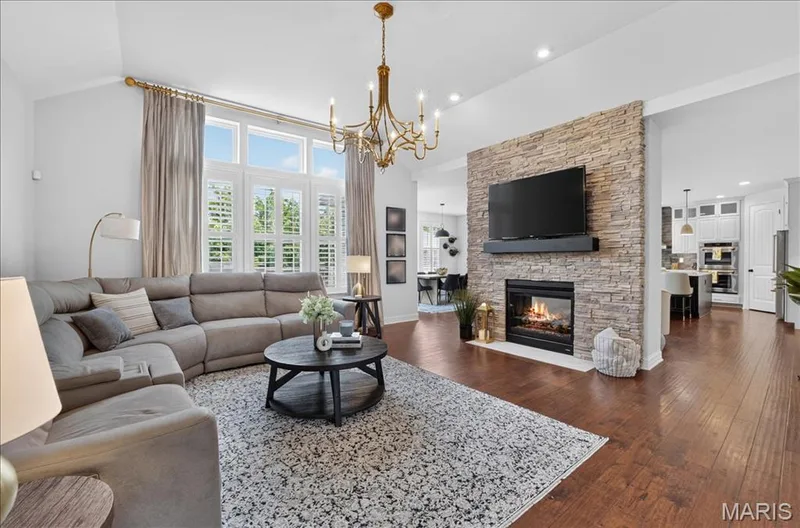 Living room featuring vaulted ceilings, wood-finish flooring, and a stacked stone fireplace with an integrated mantel — 302 Oak Stand Court, Chesterfield, MO 63005