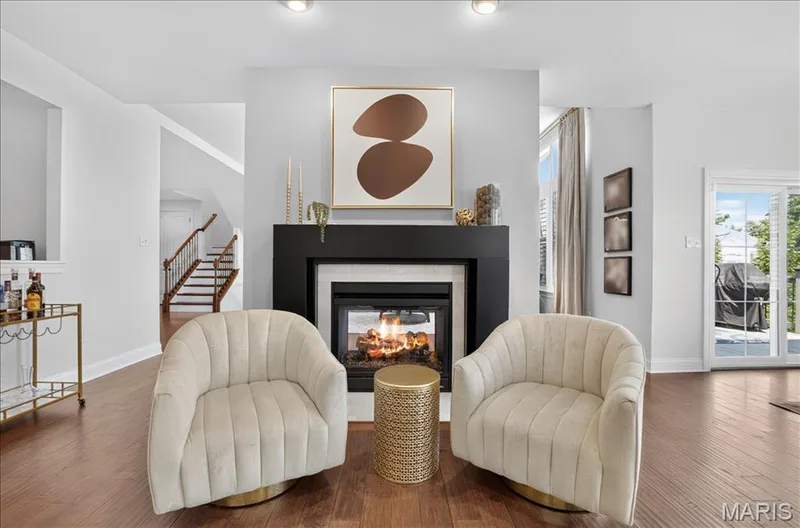 Living area featuring a floor-to-ceiling fireplace with a black mantel, an integrated firebox, wood-finish flooring, and a sliding glass door leading to the exterior — 302 Oak Stand Court, Chesterfield, MO 63005