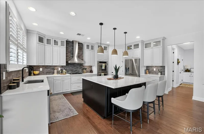 Kitchen featuring a large central island with seating, white shaker-style cabinetry, stainless steel appliances, and wood-finish flooring — 302 Oak Stand Court, Chesterfield, MO 63005