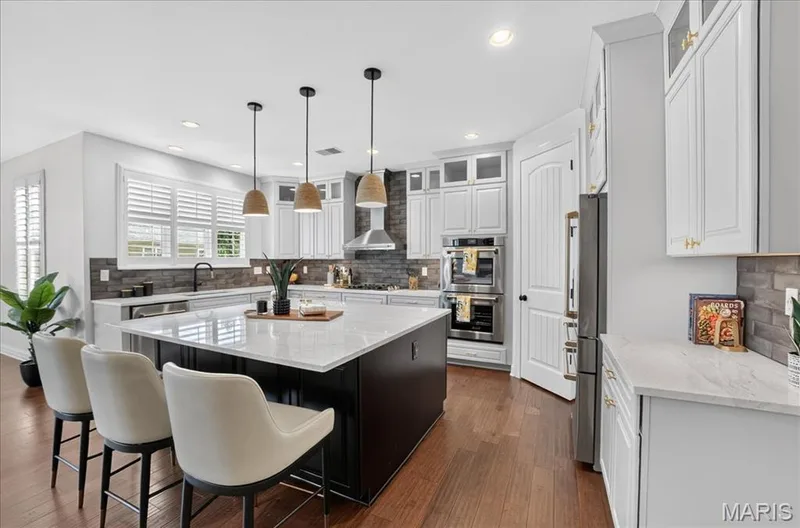 Kitchen featuring a dark-toned island with a light-toned countertop, white cabinetry with gold-toned hardware, stainless steel appliances, and wood-finish flooring — 302 Oak Stand Court, Chesterfield, MO 63005