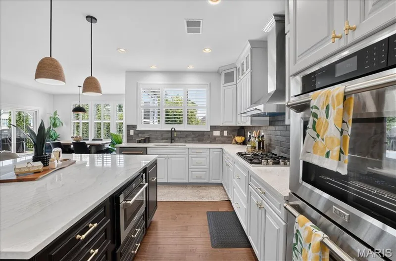 Bright kitchen featuring a substantial island with a built-in microwave, white shaker cabinetry, stainless steel appliances, a gas range, and wood-finish flooring — 302 Oak Stand Court, Chesterfield, MO 63005