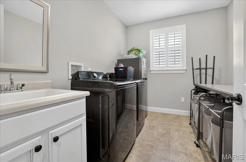 Functional laundry area featuring a white vanity with integrated sink, chrome faucet, and framed mirror — 302 Oak Stand Court, Chesterfield, MO 63005