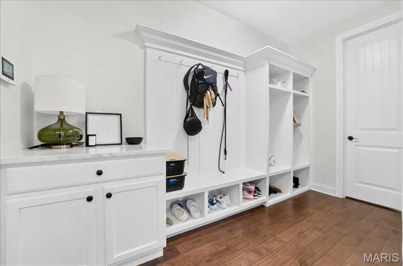 Built-in mudroom organization station featuring white cabinetry, a light-toned countertop, beadboard backing, and wood-finish flooring — 302 Oak Stand Court, Chesterfield, MO 63005