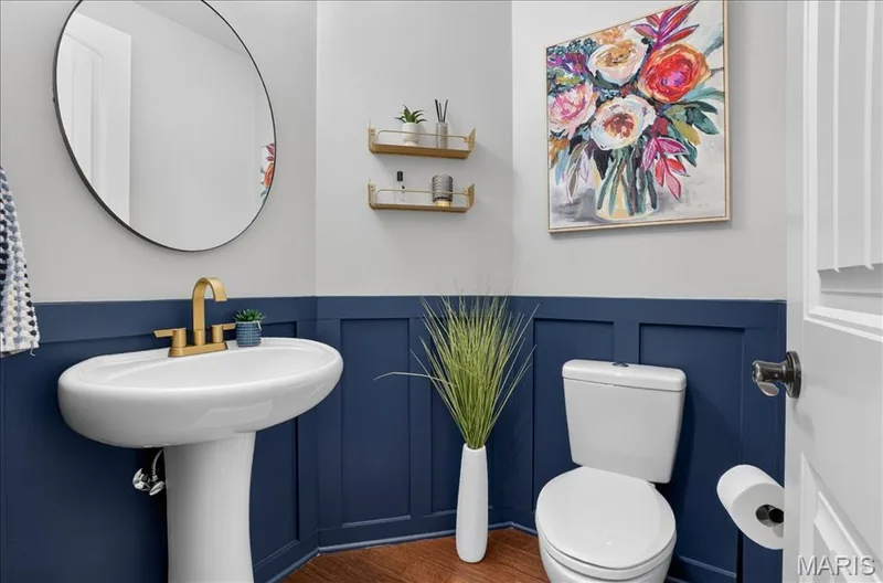Pedestal sink with brass-finish faucet, circular mirror, and wainscoting detail — 302 Oak Stand Court, Chesterfield, MO 63005
