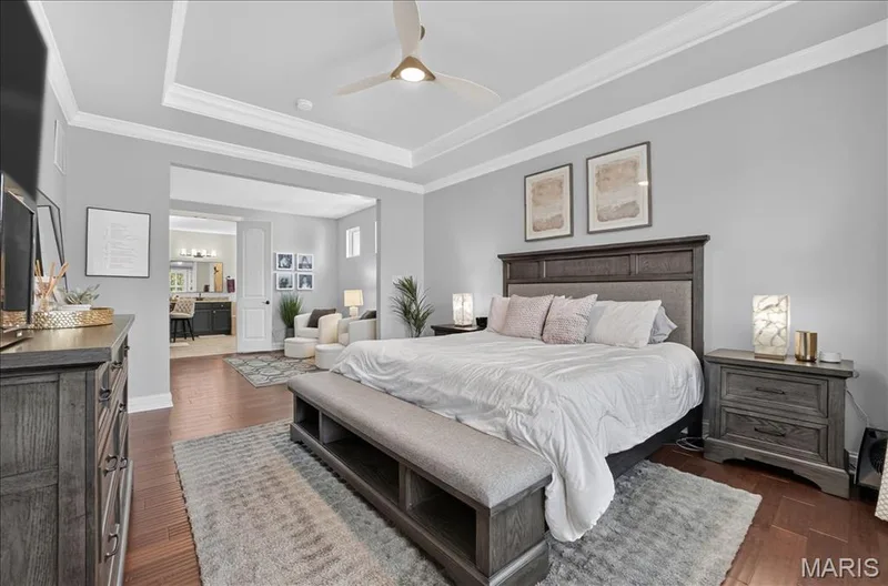 Spacious bedroom with tray ceiling, crown molding, wood-finish flooring, and a ceiling fan — 302 Oak Stand Court, Chesterfield, MO 63005