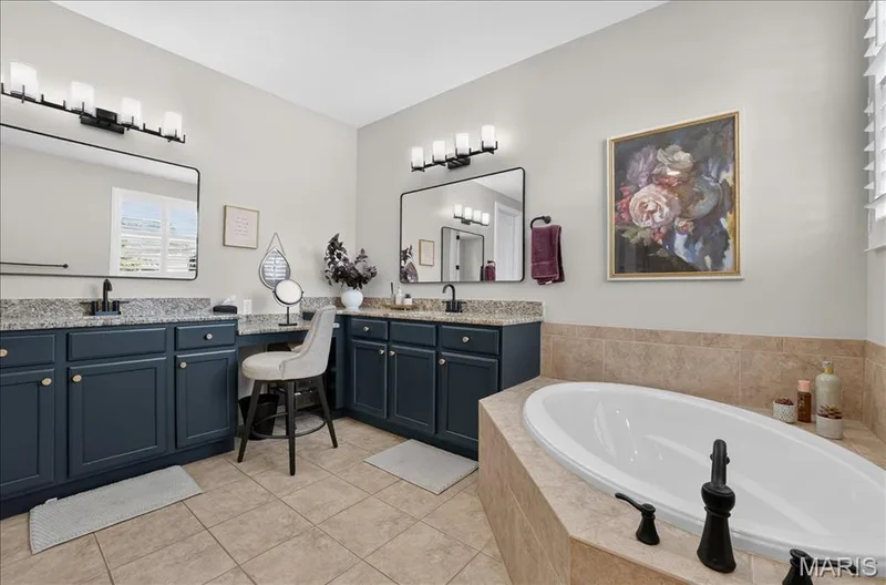 Bathroom featuring a built-in soaking tub with dark-finish fixtures, dual vanities with dark cabinetry and speckled countertops, and tile flooring — 302 Oak Stand Court, Chesterfield, MO 63005