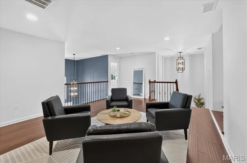Upper-level lounge area featuring wood-finish flooring, a vaulted ceiling, and dark metal balusters — 302 Oak Stand Court, Chesterfield, MO 63005