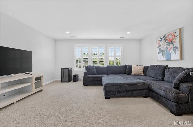 Carpeted room featuring a large window with white plantation shutters, recessed lighting, and a neutral wall color — 302 Oak Stand Court, Chesterfield, MO 63005