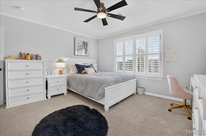 Carpeted interior room featuring a large window with white plantation shutters, crown molding, and a ceiling fan with integrated lighting — 302 Oak Stand Court, Chesterfield, MO 63005
